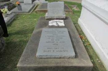 The grave includes the original headstone as the middle feature, between the newer headstone and memorial stone.